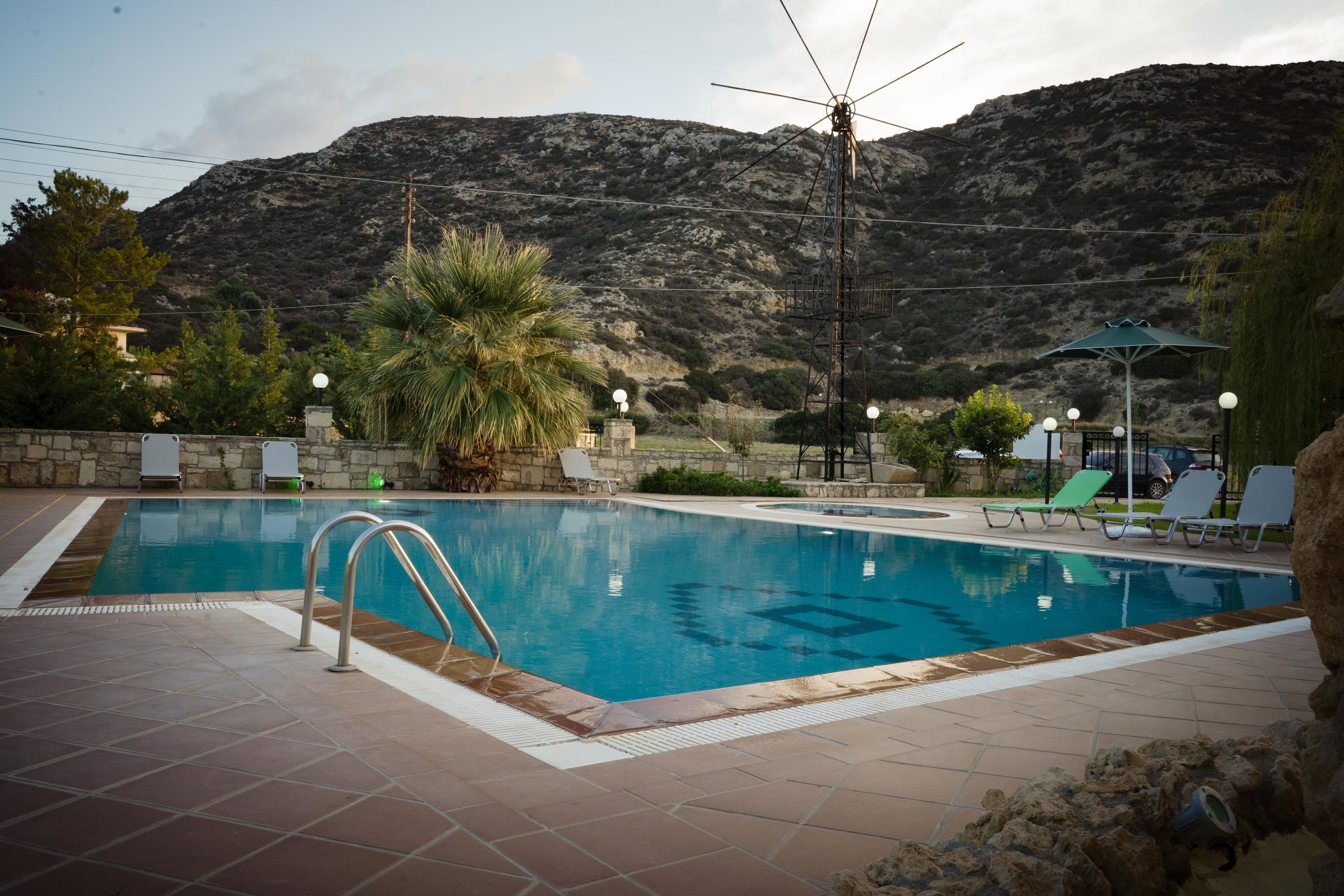 A swimming pool with a view of mountains, surrounded by lounge chairs and a palm tree.