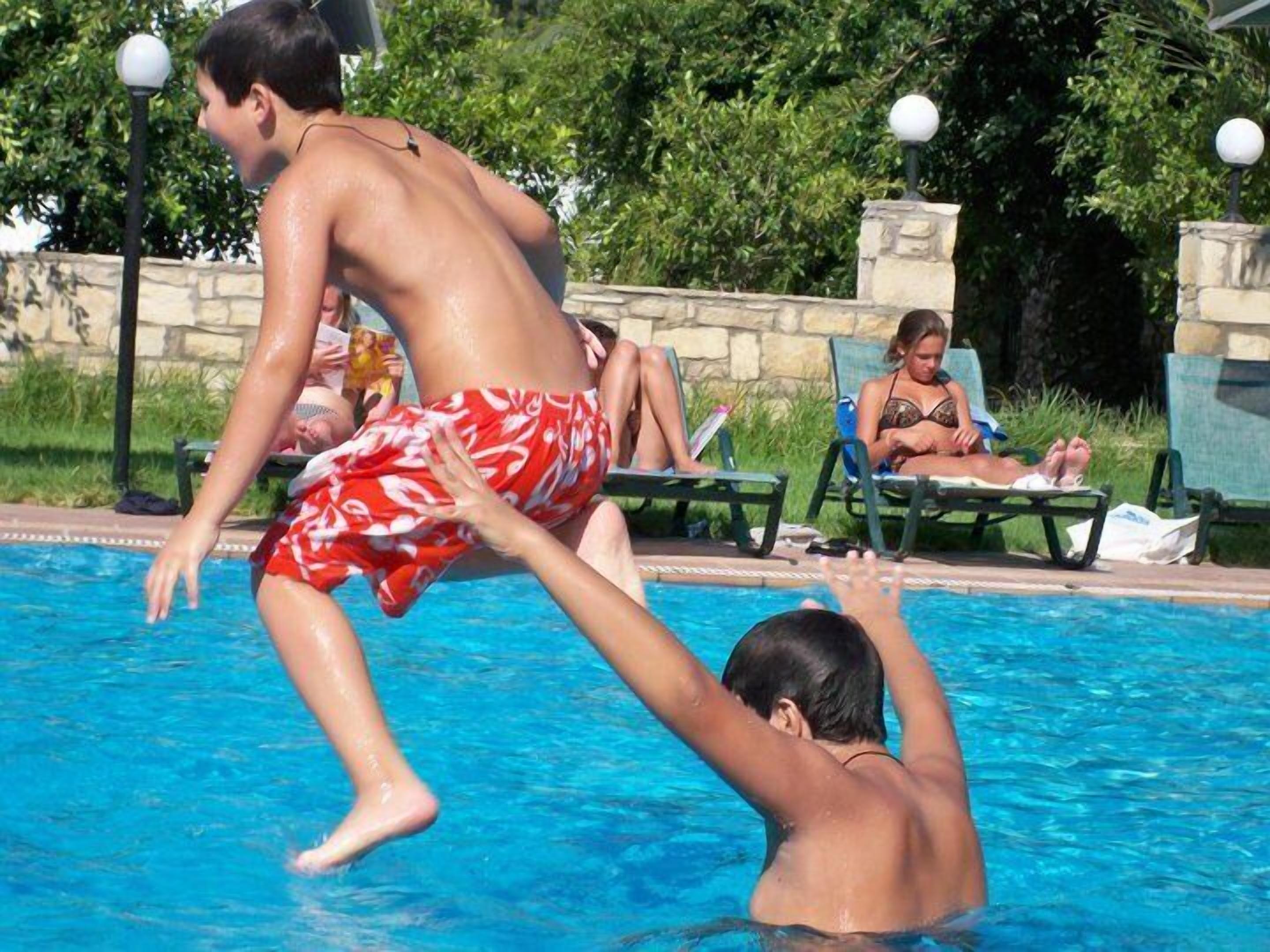 Una piscina con gente nadando y sentada en el borde.