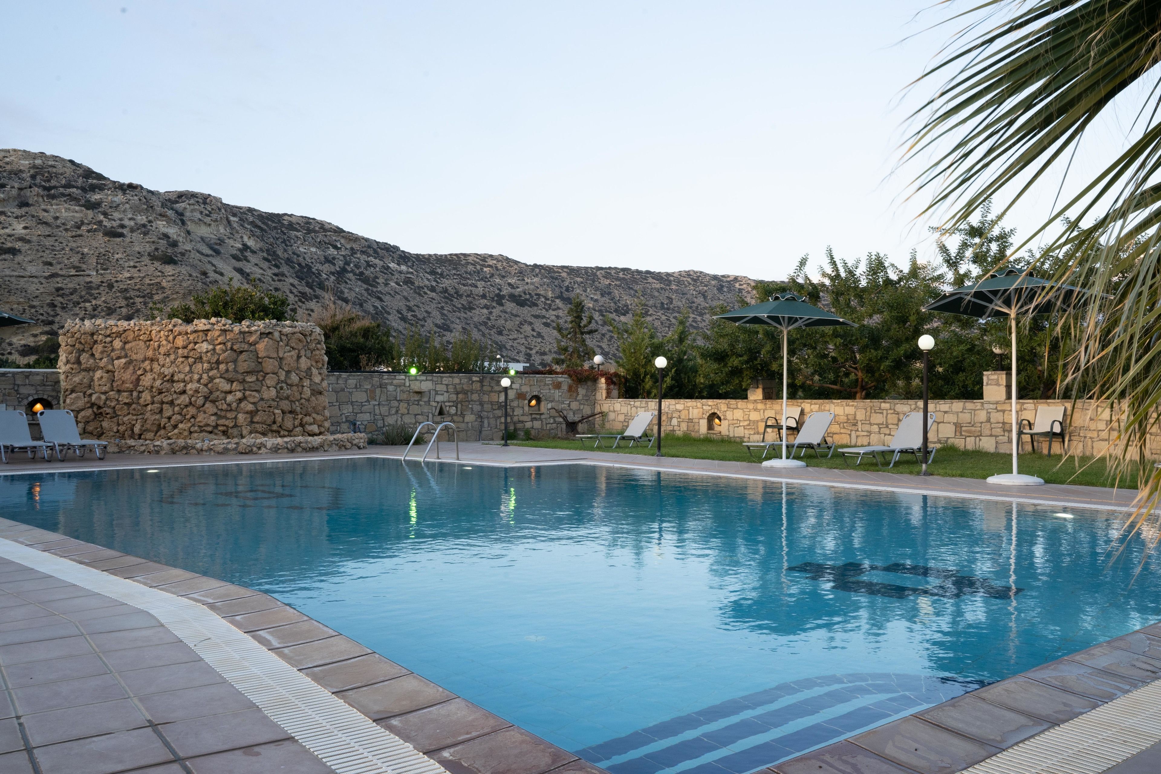 Une piscine entourée de chaises longues et d’un mur de pierre, le tout niché au cœur d’un paysage montagneux.