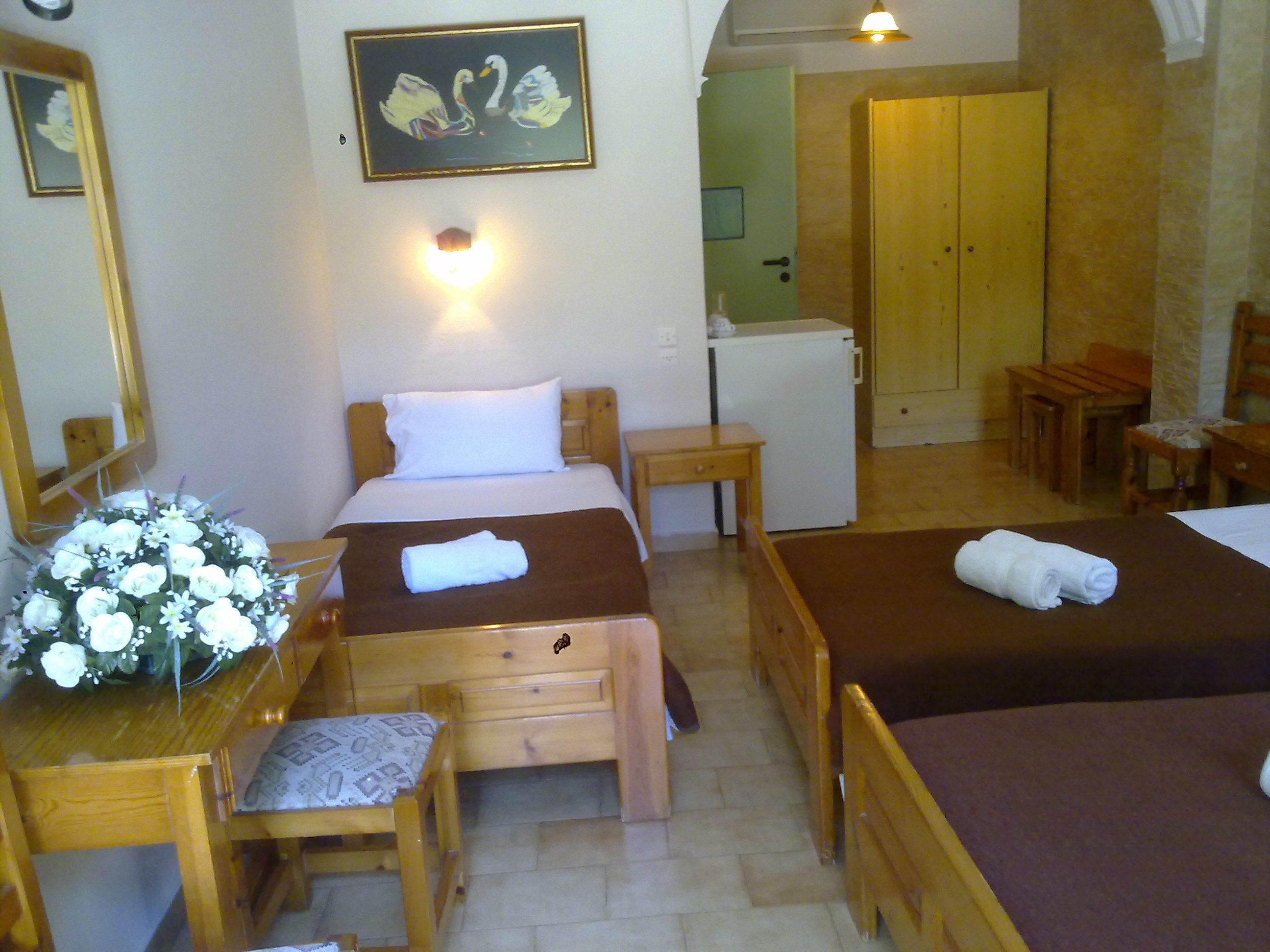 A hotel room with two beds, a desk, a chair, a small table, a refrigerator, and a mirror.