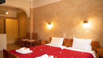 Habitación de hotel con dos camas, cabeceros de madera y una pared de piedra. Hay dos mesitas de noche, un armario de madera y un escritorio con sillas.