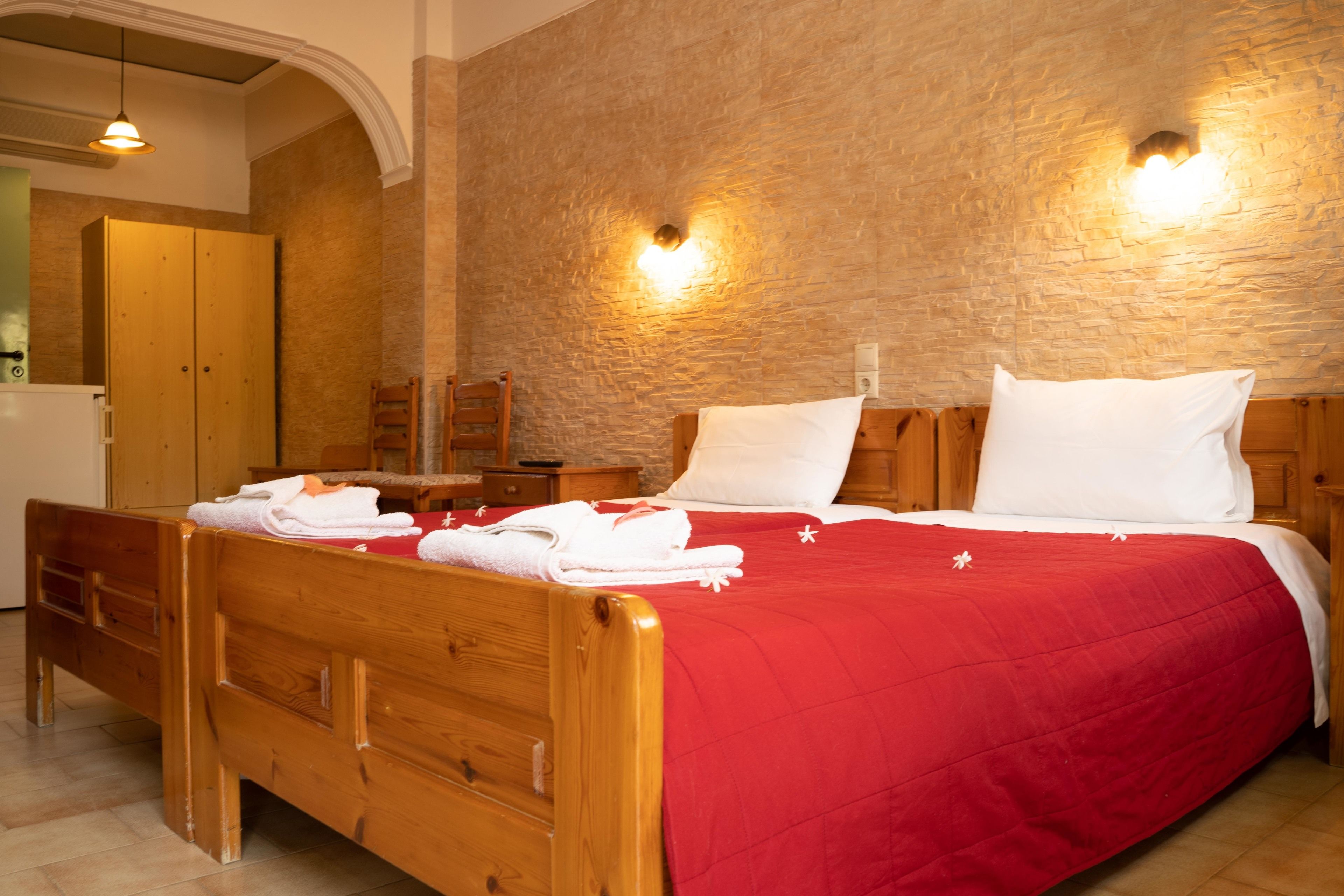 A wooden bed with a red bedspread, a wooden nightstand, and a mirror above the bed.