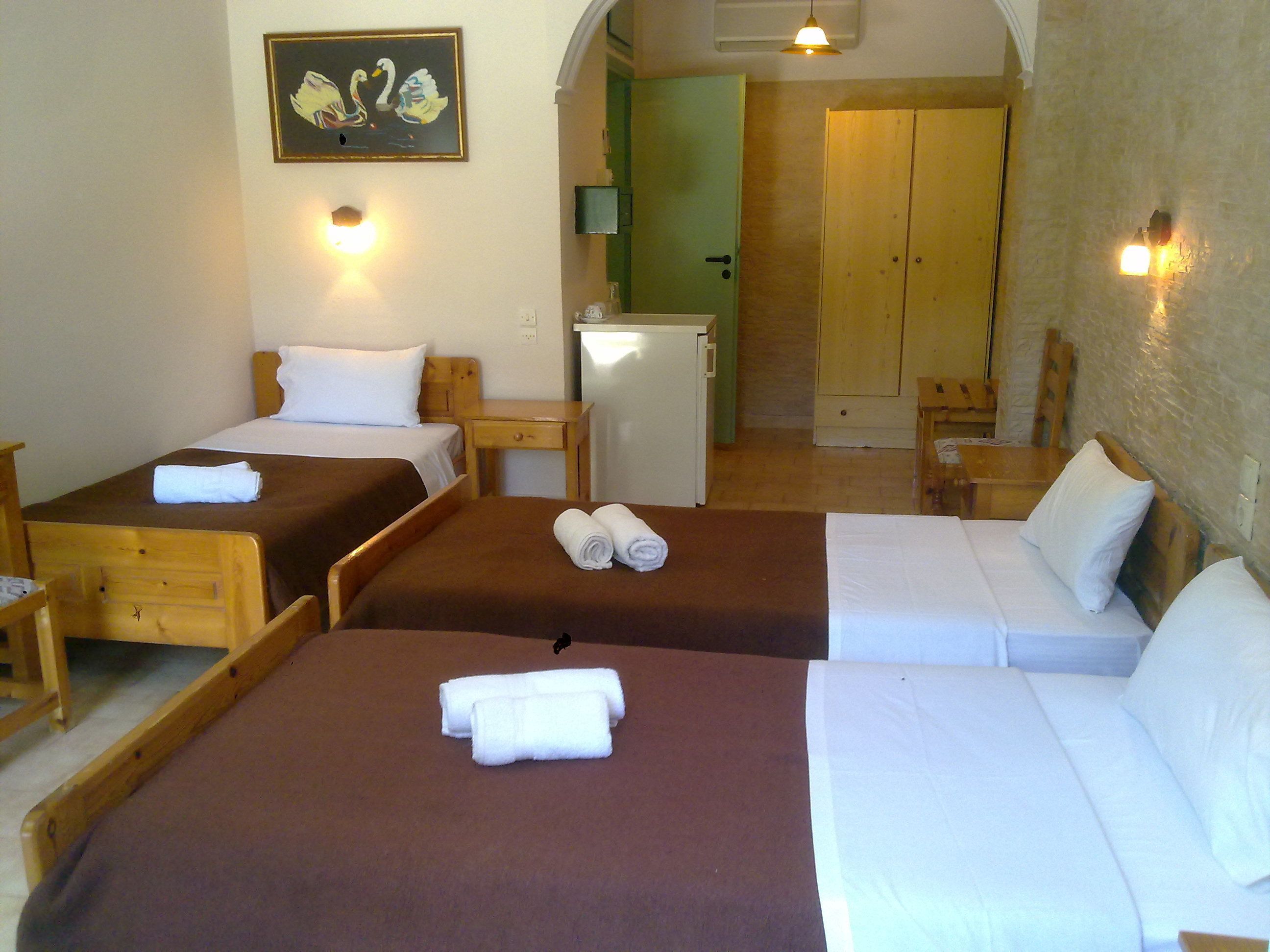 Quarto de hotel com duas camas de solteiro, uma cama de casal, um kitchenette pequeno e um guarda-roupa de madeira.