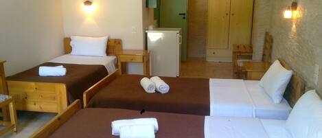 Quarto de hotel com duas camas de solteiro, uma cama de casal, um kitchenette pequeno e um guarda-roupa de madeira.