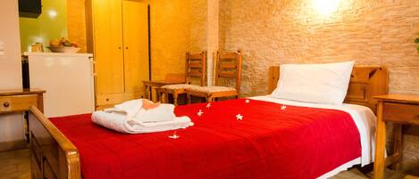 A hotel room with a red bedspread, wooden furniture, a small table, a chair, and a wall-mounted light fixture.