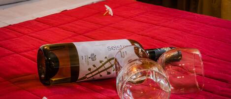A bed with a red quilt, a bottle of Sejstrup wine, and two empty wine glasses on it.