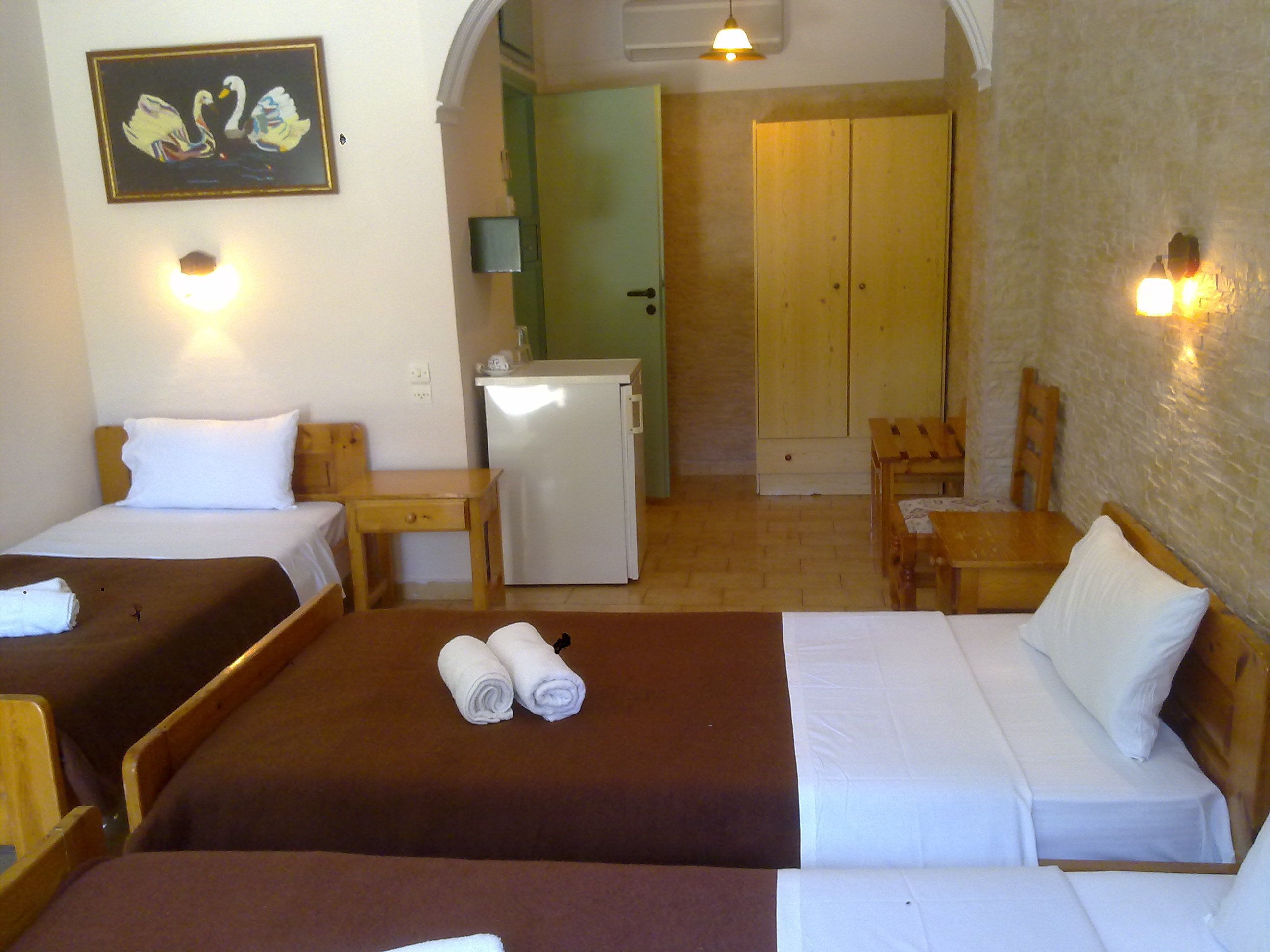 Une chambre d’hôtel avec deux lits, un petit bureau, un réfrigérateur et une armoire en bois.