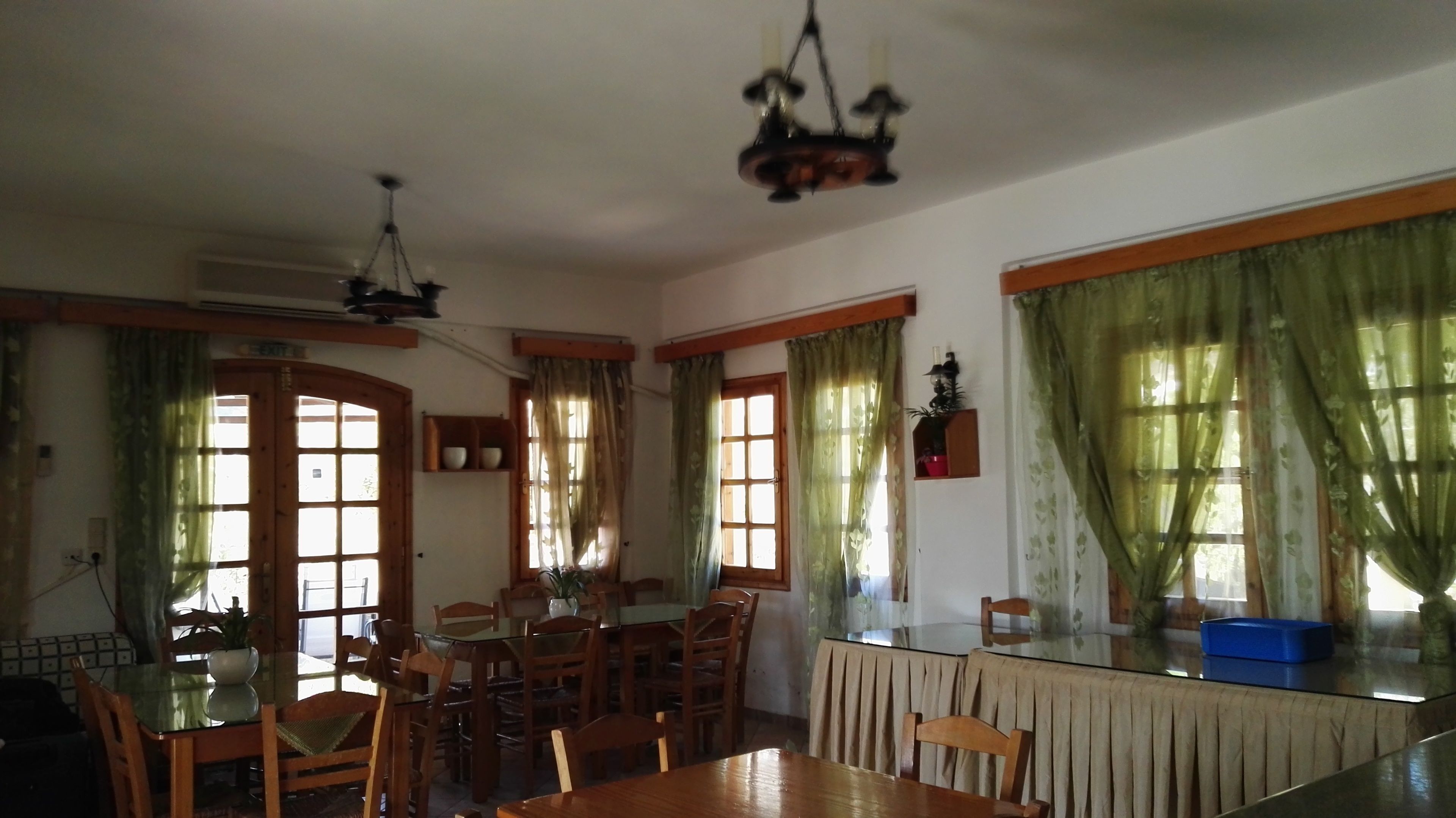 A dining area with a glass table, wooden chairs, a chandelier, and green curtains.
