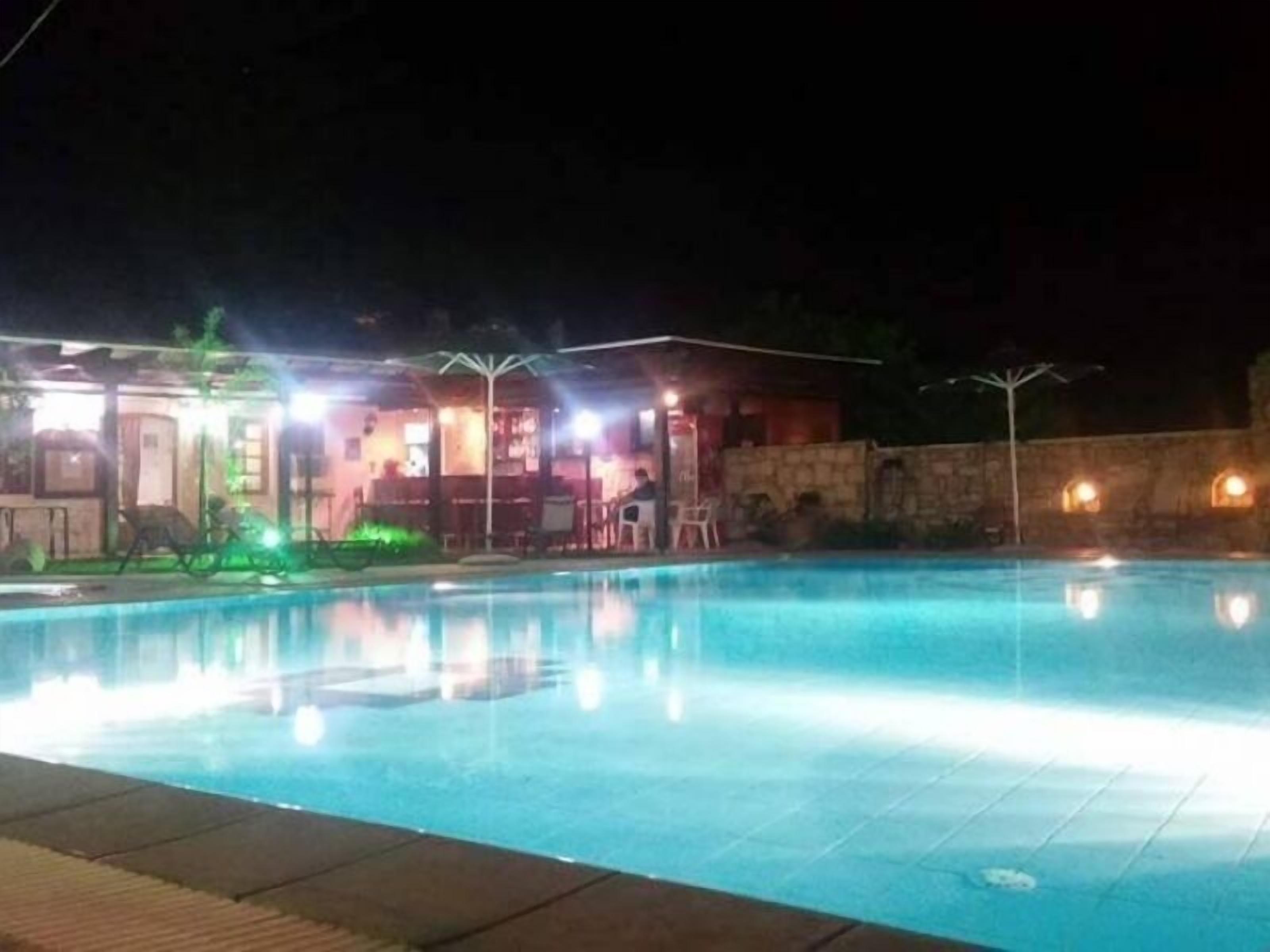 Ein Nachtblick auf ein Schwimmbecken mit überdachtem Bereich und Sitzgelegenheiten.