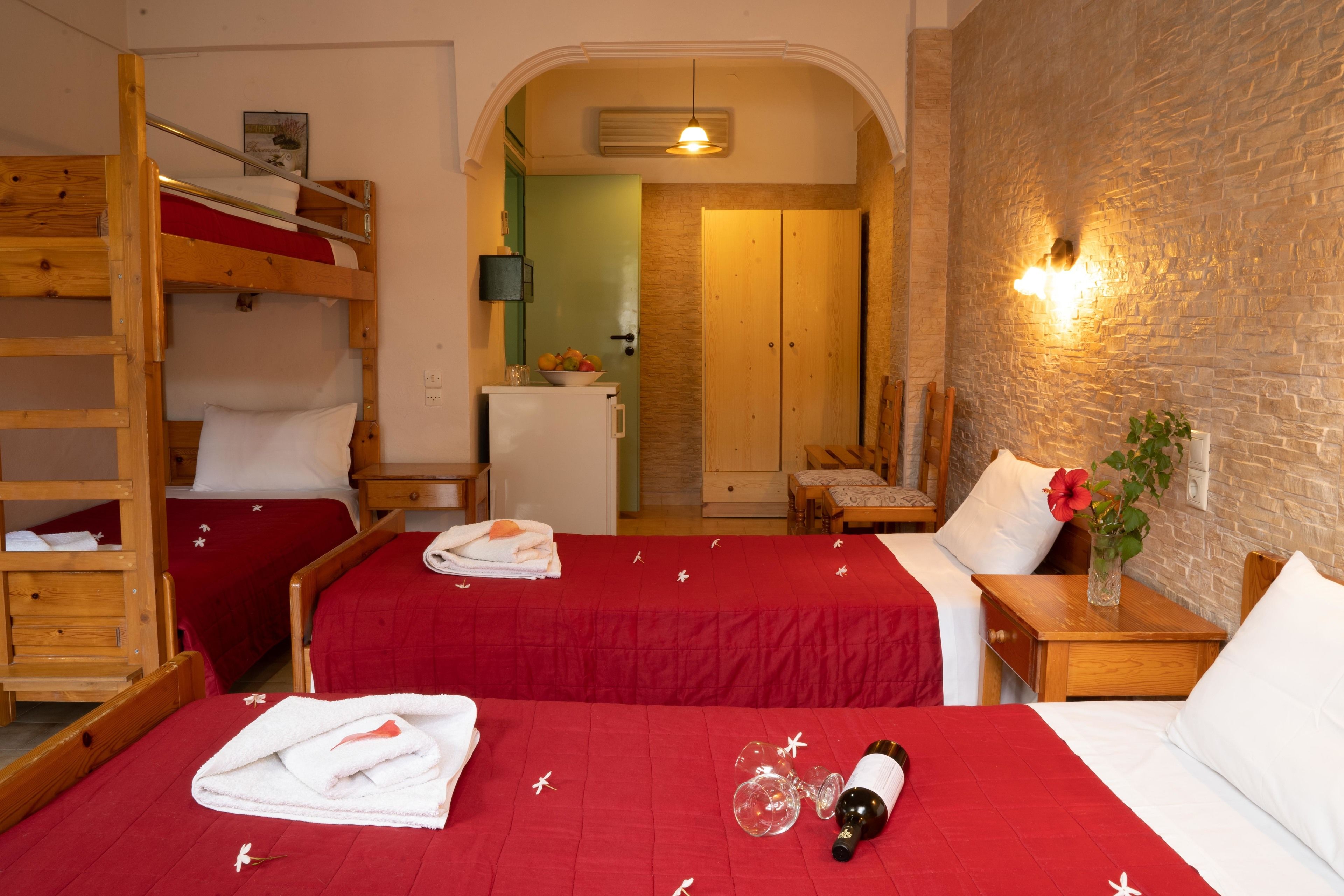 A hotel room with two beds, a wooden bunk bed, a small kitchenette, and a brick wall.