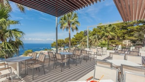 An outdoor dining area with tables and chairs, overlooking a scenic view of the sea and mountains. - Sun Club El Dorado (Llucmajor)