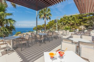 Un espacio de comedor al aire libre con mesas y sillas, con vistas panorámicas al mar y a las montañas.