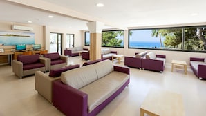 A modern living room with a large sofa, armchairs, and a coffee table. There is a desk with a computer and a TV. The room has large windows with a view of the ocean. - Sun Club El Dorado (Llucmajor)