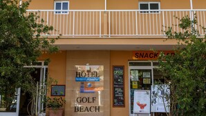 Un hôtel à plusieurs étages, avec une enseigne indiquant « Golf Beach » et un « bar à collations » à l’entrée.