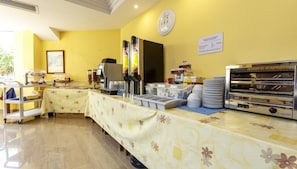Disposição de buffet de café da manhã, com máquina de café, dispensadores de suco e diversas opções de alimentos.