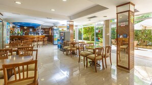 Un vaste espace intérieur aménagé en salle à manger, avec de nombreuses tables et chaises en bois, un comptoir de bar et une grande fenêtre donnant sur l’extérieur.
