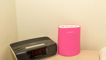 A digital clock and a pink speaker on a bedside table.
