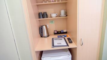 A small kitchenette with a coffee maker, tea pot, cups, and a microwave.