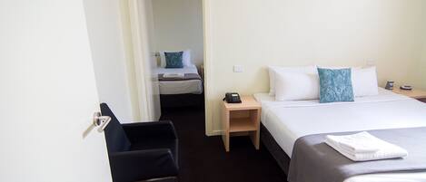 Habitación de hotel con cama, una silla, mesita de noche y puerta que da a otra habitación.