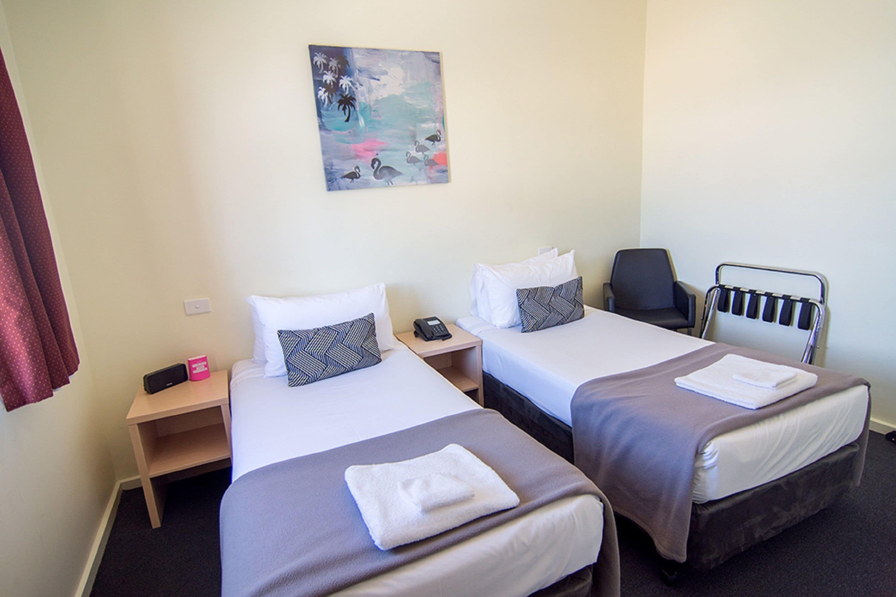 A hotel room with two beds, a painting on the wall, a chair, and a bedside table with a phone.