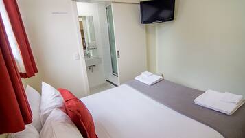 Habitación de hotel con cama, televisión montada en la pared y baño visible a través de una puerta abierta.