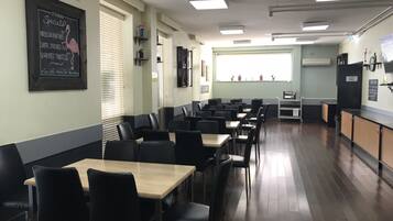 Un restaurant avec des chaises noires et des tables en bois, un menu écrit à la craie sur le mur et une fenêtre avec des stores.