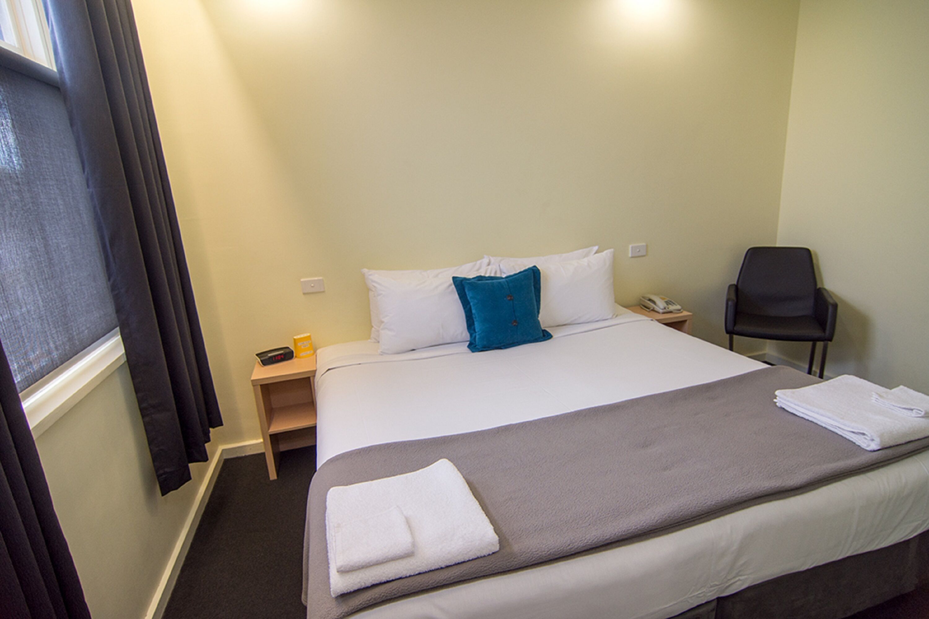 A hotel room with a bed, a chair, a nightstand, and a window with curtains.