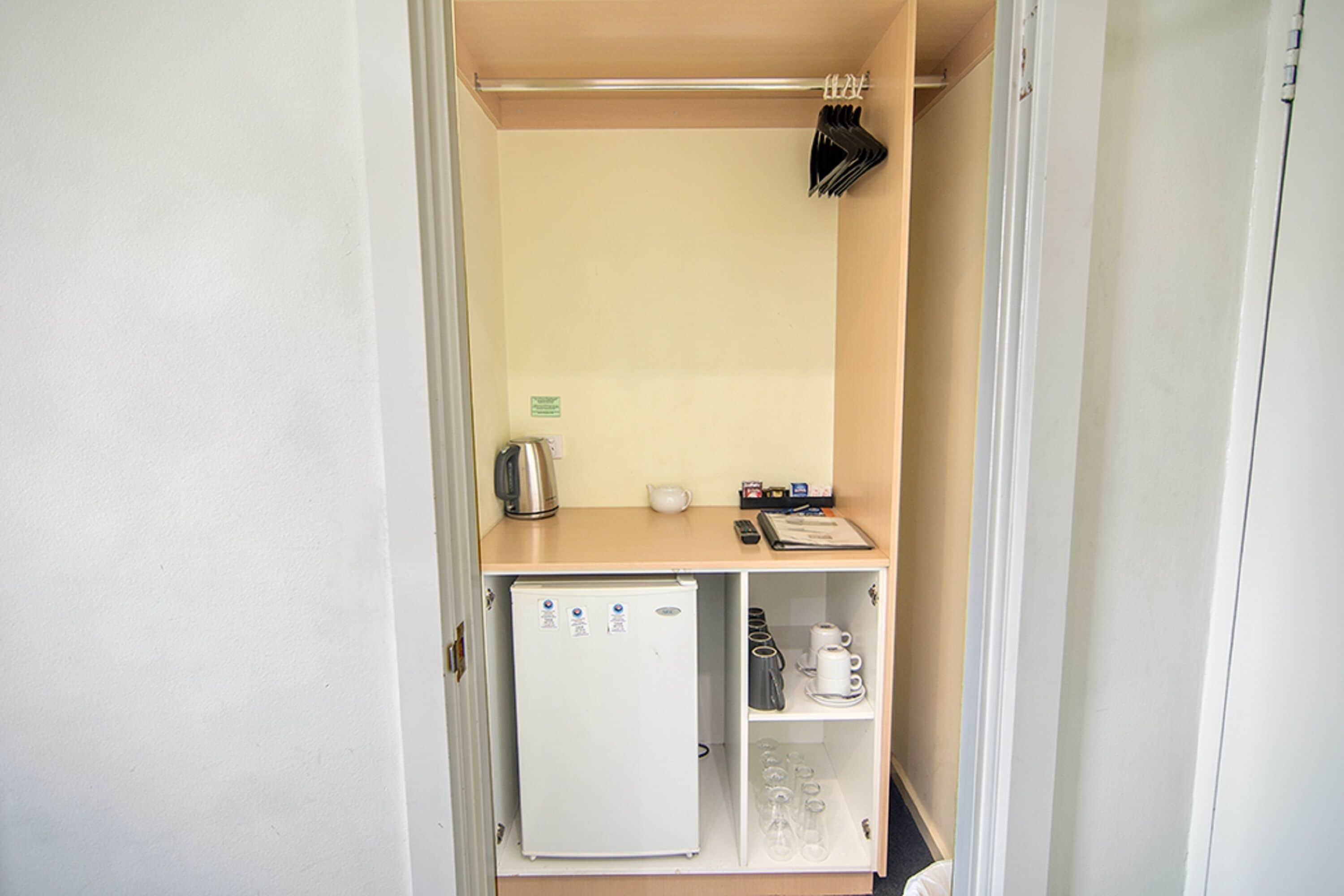 Una kitchenette compacta con un refrigerador, una cafetera y una tetera sobre la encimera.