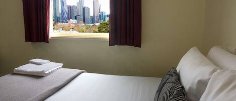 Habitación de hotel con cama, ventana con cortinas y vista del horizonte urbano, además de una toalla doblada sobre la cama.
