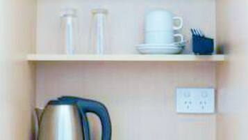 Una cocina equipada con hervidor, cafetera y una pequeña mesa con un control remoto.