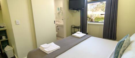 A hotel room with a bed, a TV mounted on the wall, a window with curtains, and a bathroom visible through an open door.