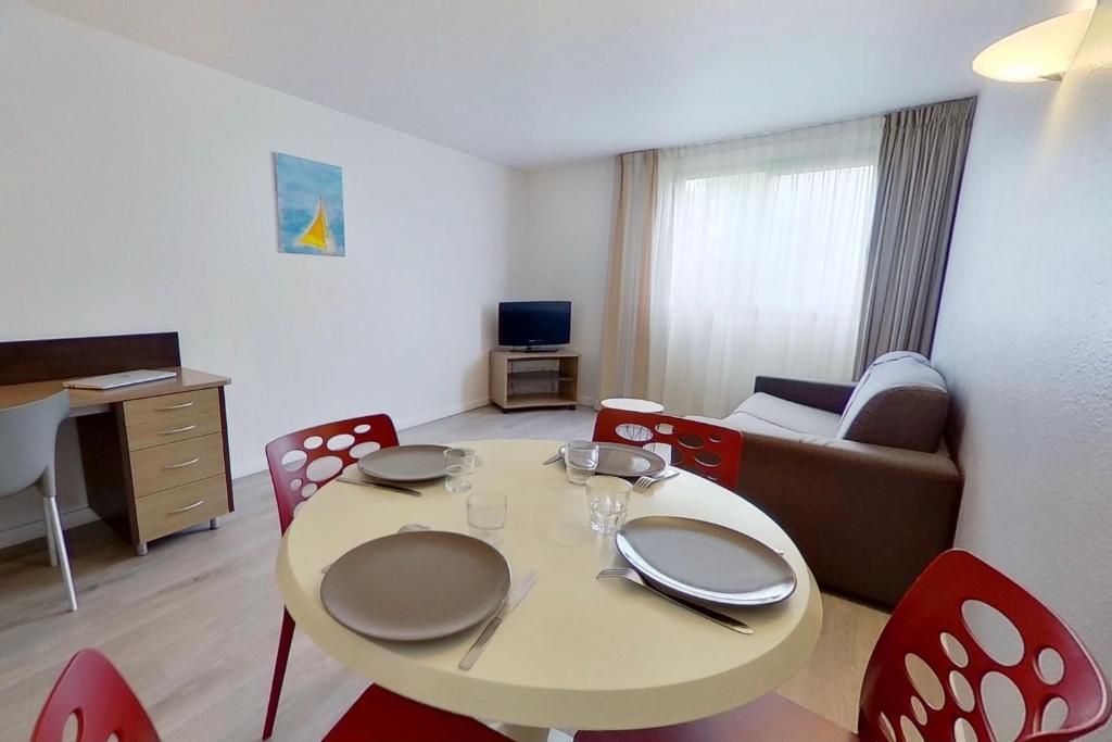 Un ambiente compatto con tavolo da pranzo per due persone, divano, televisore e scrivania.