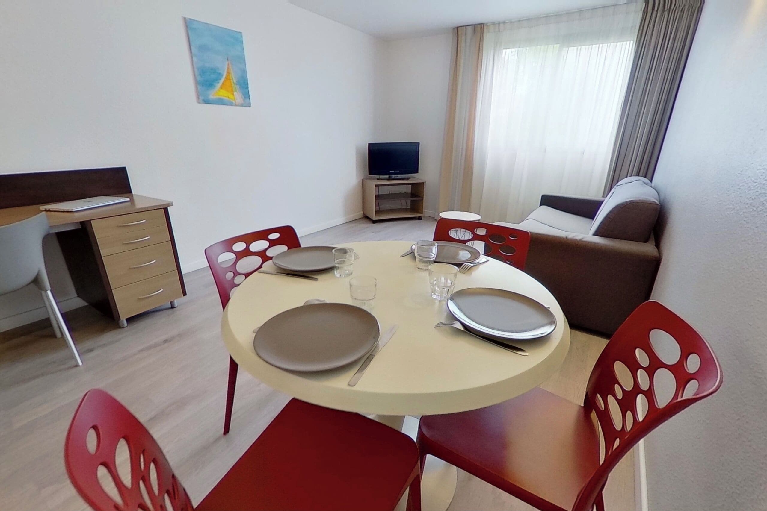 A dining area with a round table, red chairs, and a television in the corner.