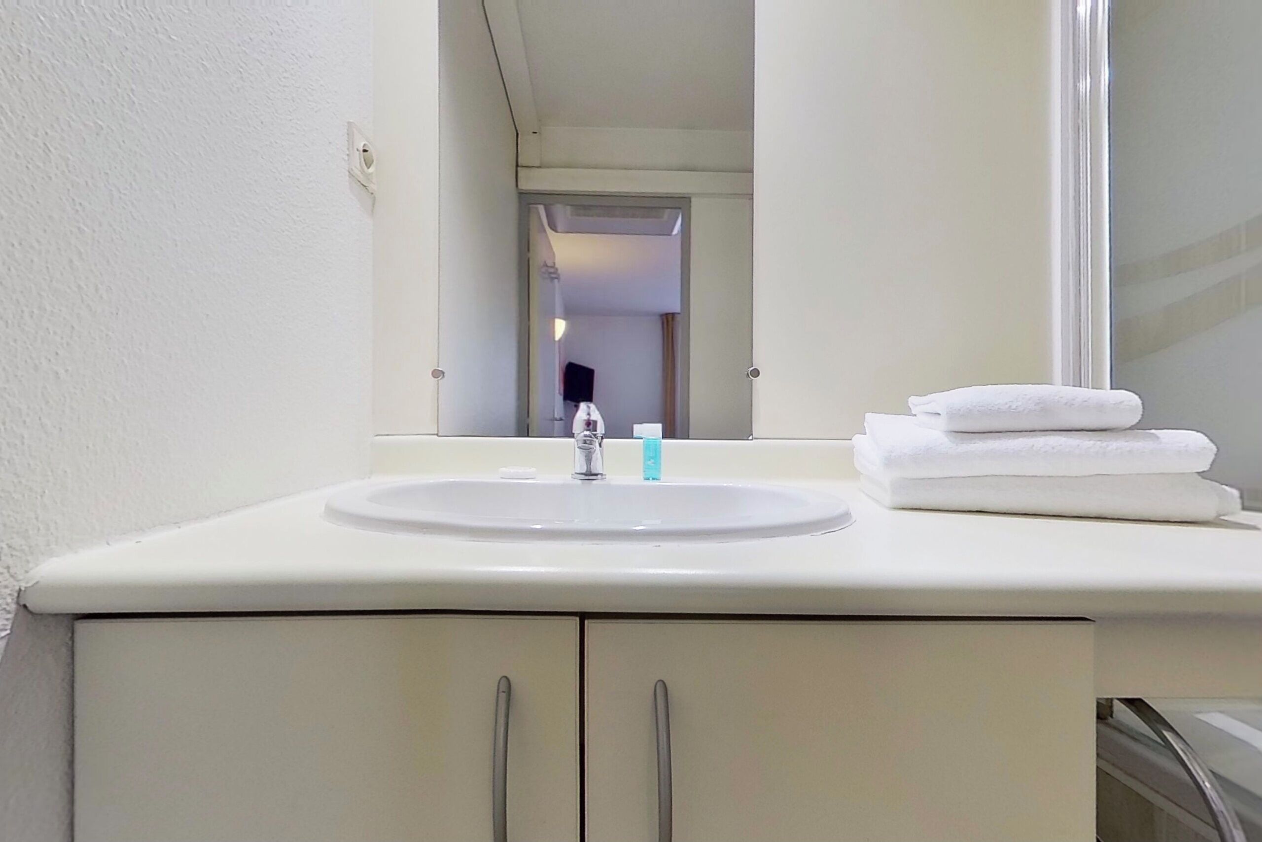 A bathroom with a white sink, a mirror, and a towel stacked on the counter.