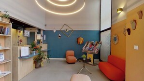 A modern reception area with a blue wall, orange seating, and a desk with a plant. - City Residence Aix En Provence (Aix-en-Provence)