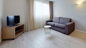 A modern living room with a flat-screen TV on a wooden stand, a grey sofa, and a small round table. - City Residence Aix En Provence (Aix-en-Provence)