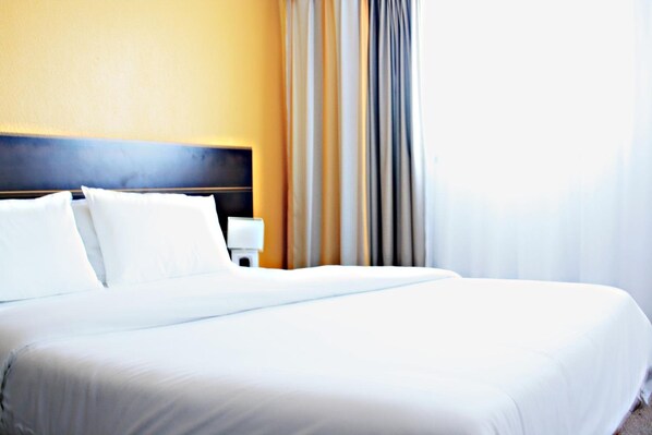 Una habitación de hotel con una cama grande, una mesita de noche y una ventana con cortinas.