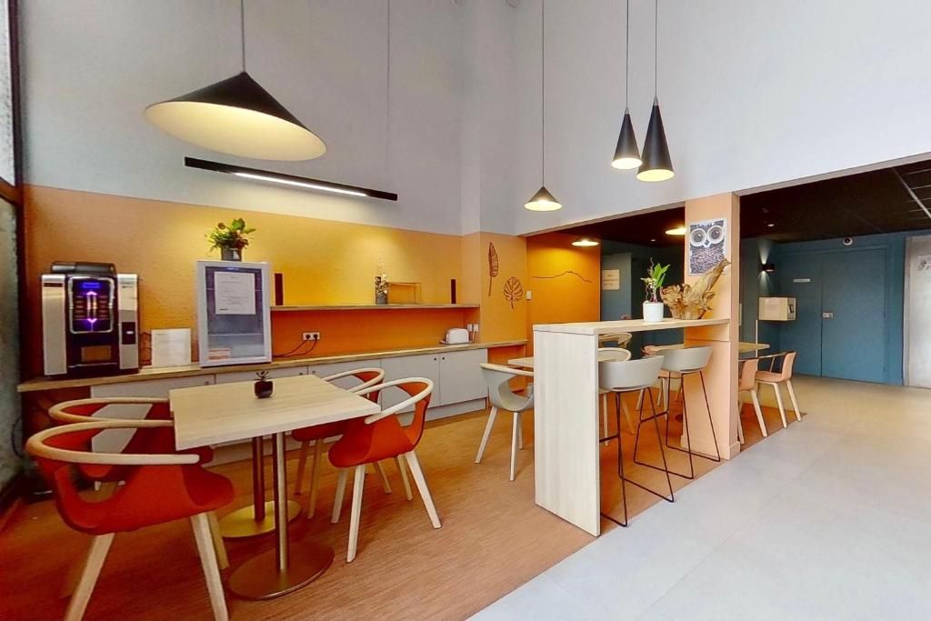 A modern kitchen with a dining area, featuring pendant lighting, a coffee machine, and a plant.