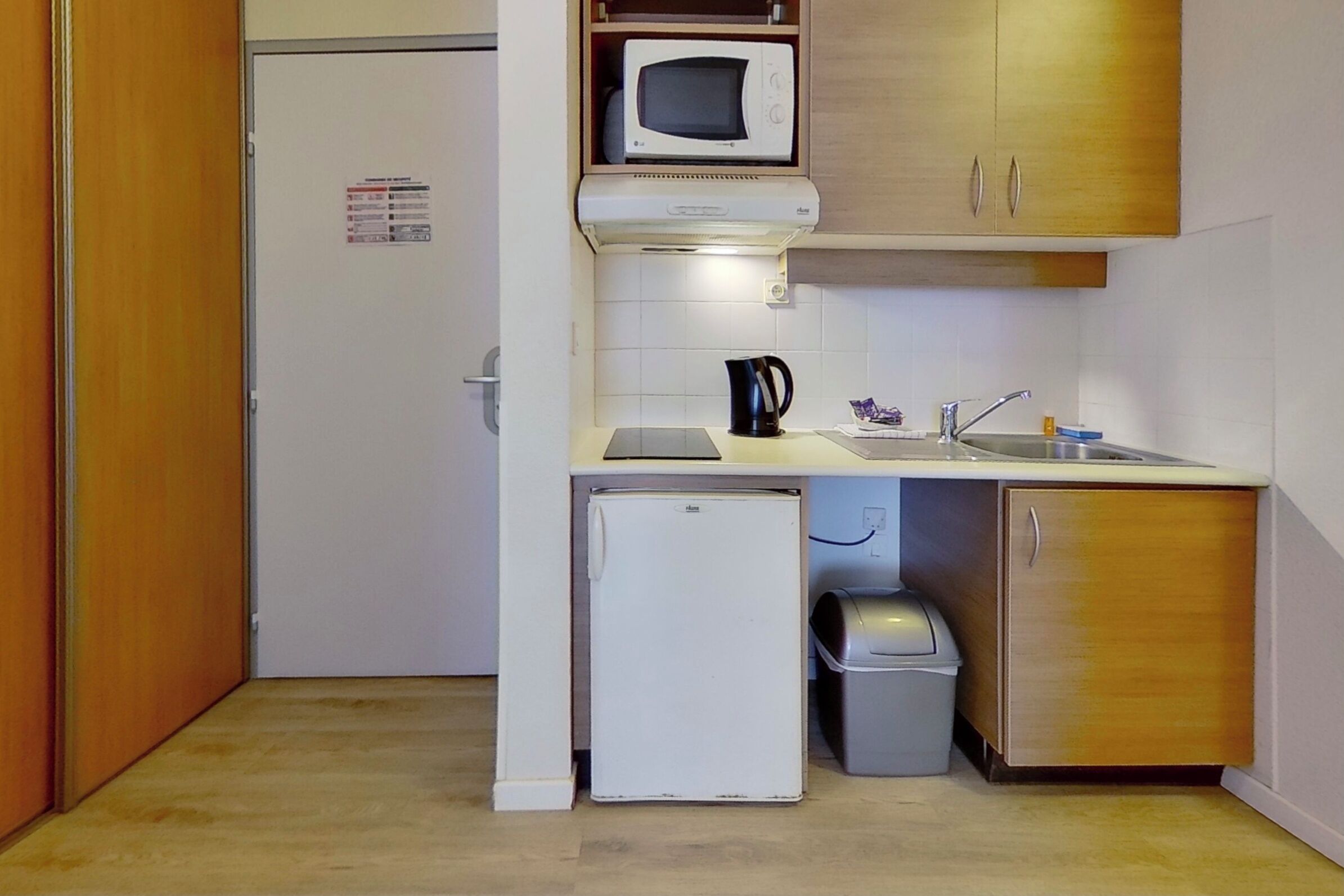 Une cuisine compacte équipée d’un four à micro-ondes, d’un petit réfrigérateur, d’un évier et d’une poubelle.