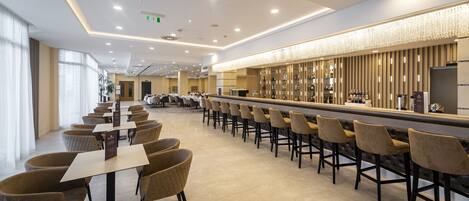 A modern hotel lobby with a long bar, seating area, and a reception desk.