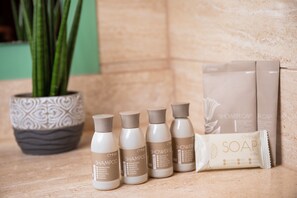 A bathroom with a potted plant, a shower cap, and bottles of shampoo and soap. - Greenfield Hotel Golf & Spa (Buk)