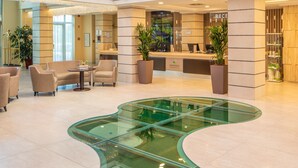 A hotel lobby with a reception desk, seating area, and a glass-bottomed pool. - Greenfield Hotel Golf & Spa (Buk)