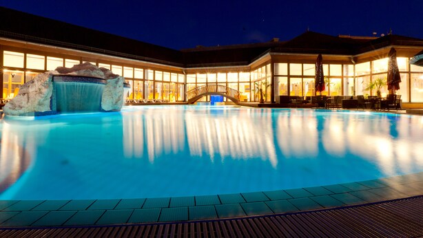 A large indoor swimming pool with a hot tub, surrounded by a building with large windows and a covered seating area. - Greenfield Hotel Golf & Spa (Buk)