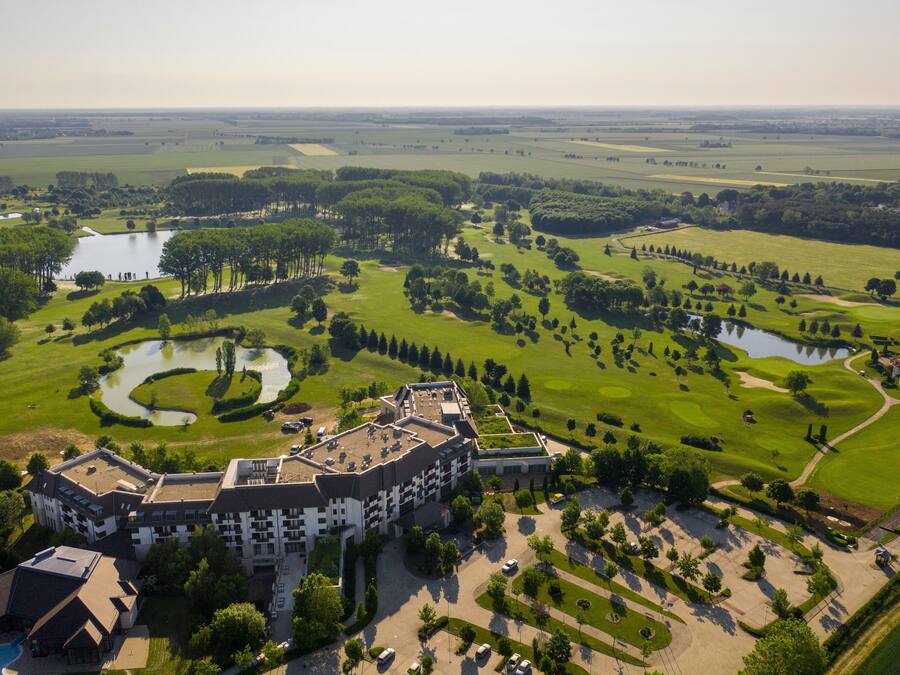 Vista aérea de un campo de golf con un club de campo, estanques y un edificio grande de varios pisos.