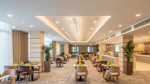 A spacious hotel lobby with multiple dining areas, large windows, and a modern chandelier. - Greenfield Hotel Golf & Spa (Buk)