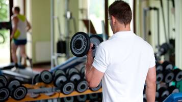 Un gimnasio con un hombre levantando pesas, una mujer ejercitándose y diversos equipos de entrenamiento.