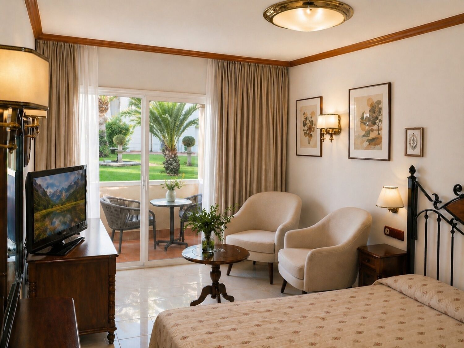 Een hotelkamer met een bed, twee fauteuils, een tafeltje, een televisie en een balkon met uitzicht op palmbomen.