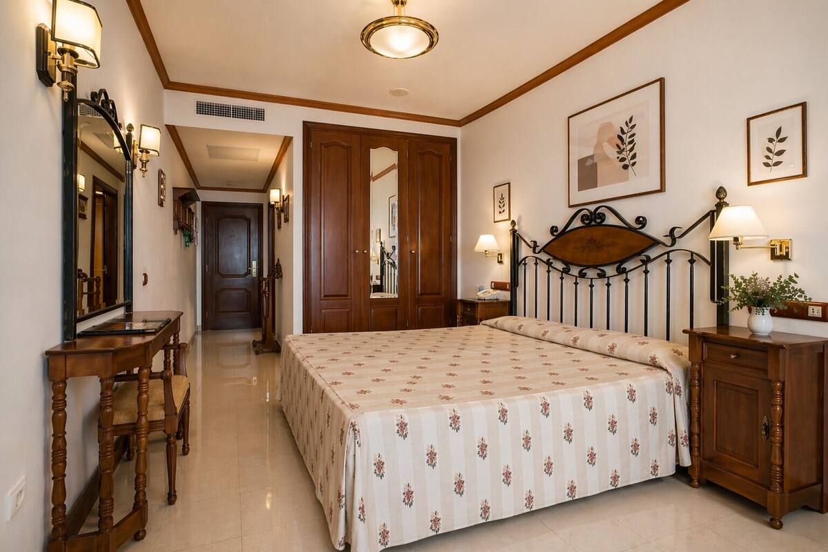 Une chambre d’hôtel équipée d’un lit, de tables de chevet, d’un bureau, d’un miroir et d’œuvres d’art encadrées accrochées aux murs.