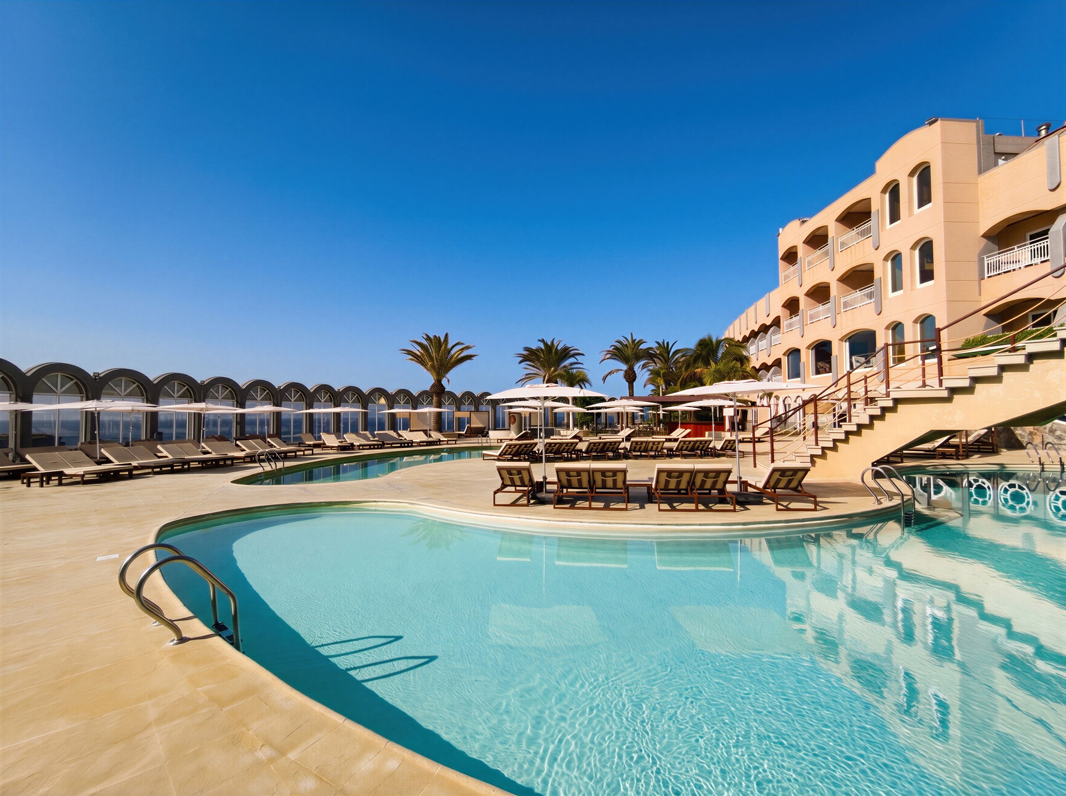 Une piscine d’hôtel avec des chaises longues, des parasols et un bâtiment doté de balcons.