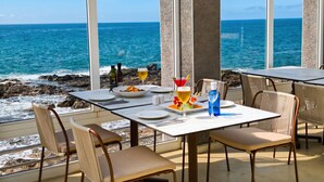 Ein Restaurant am Meer mit Terrassensitzgelegenheiten, Blick auf den Ozean und einem Tisch mit Essen und Getränken.